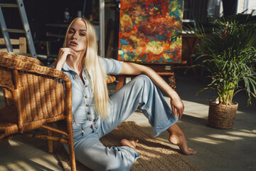 Glamour woman with blond hairs in styled jeans clothes posing lying down on carpet leaning on chair...