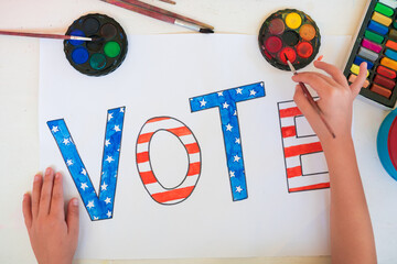 Close-up of a child girl drawing the word Vote. Vote symbol in the American elections. Political...
