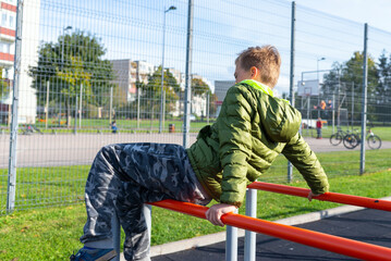 Sports child in the autumn on playground. gymnastic exercises outside. boy overcoming efforts.