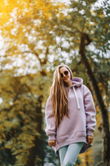 Beautiful happy smiling young woman wearing pink hoodie walking in autumn park. Season and people concept.