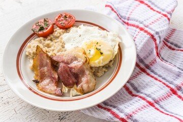 English breakfast with oatmeal, bacon, scrambled eggs and tomatoes.