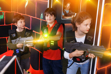 Group of friendly smiling teenagers with laser guns having fun on dark lasertag arena
