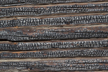 Close-up of charred walls of a wooden blockhouse. The old charred wall of the house. Horizontal lines. Wood wall texture after fire