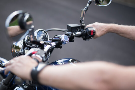 View of a male active senior man riding his bike looking down at the handlebars of his motorbike cycle chrome guages mirros hand instrumentation outdoors on a bright day