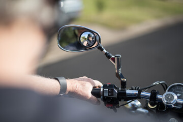 View of a male active senior man riding his bike looking down at the handlebars of his motorbike cycle chrome guages mirros hand instrumentation outdoors on a bright day