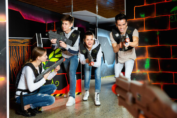 Modern pleasant cheerful smiling people with laser pistols playing laser tag on dark labyrinth