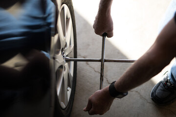 Obraz premium View of a man changing a wheel on a car tightening nuts lit by natural light from nearby door service repair maintain check shadows