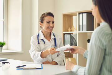 Fototapeta premium Smiling doctor therapist giving madical prescription to patient during consultation in medical clinic