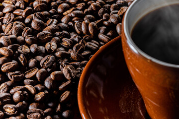 カップに入った湯気の立つ熱いコーヒーと背景のコーヒー豆
