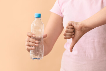 Woman with plastic bottle showing thumb-down gesture on color background. Ecology concept