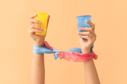 Female hands with plastic cups on color background. Ecology concept