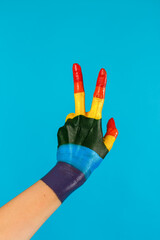 close-up hand painted as rainbow flag shows victory gesture on a blue background. LGBT topics, lesbians, gays, transgender, bisexual.