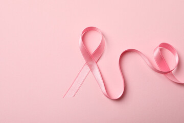 Pink awareness ribbon on pink background, close up