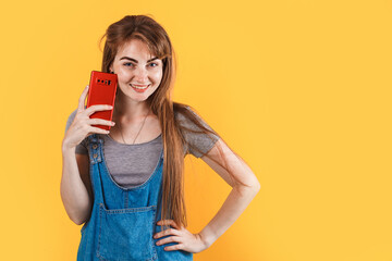 caucasian woman in a denim dress looking straight and talking on the phone. isolated on a yellow orange background. copy space