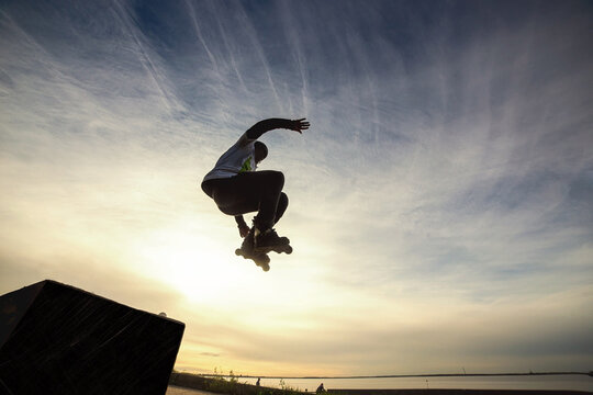 Unrecognizable roller on the extreme roller skates performing acrobatic jump at sunny sky - Guy at extreme sport competition on sunny afternoon - Alternative lifestyle concept on warm sunshine colors