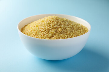 Bowl with raw couscous on blue background