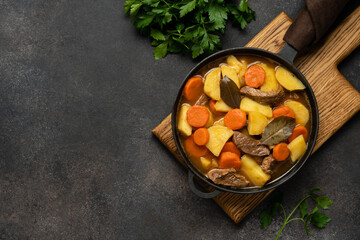 Stew with carrots and potatoes in cast iron skillet on dark brown concrete background. Seasonal home cooking