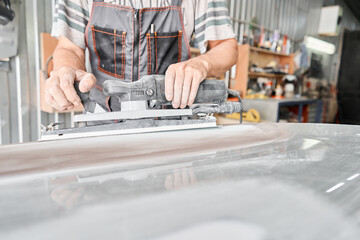 The mechanic works with a grinding tool. Sanding of car elements. Garage painting car service. Repairing car section after the accident.