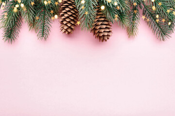 Christmas border with fir branches and conifer cones on pastel pink background