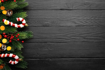 Fototapeta na wymiar Christmas or New Year decoration background - fir tree branches, rowan and candy cane on black wooden background