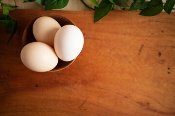 Three fresh white eggs in a wooden cup on a wooden table with some green plants
木製テーブルの上にある木のカップに入った３つの白い卵とグリーン
