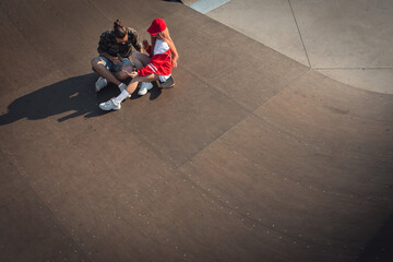 Young couple hangout in skate park while sitting on skateboard.