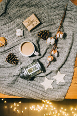 Fototapeta na wymiar Flat lay. Cup of coffee, a branch of cotton, a candlestick and cones on a gray knitted plaid.