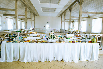 Large wedding area with a variety of colored sweets on the table in a bright room with wooden beams.