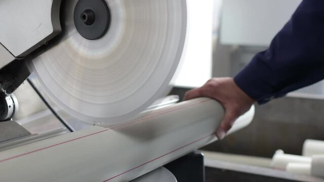 Factory industry worker cutting polypropylene pipe with circular saw. Warehouse of polypropylene pipes. Workshop with extruders for producing plastic pipes.