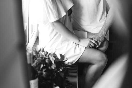 Cropped image of the groom hugging the bride sitting on the windowsill in the morning.