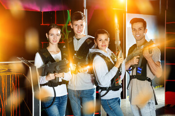 Fototapeta na wymiar Happy pleasant cheerful positive smiling young people with laser pistols posing together on dark laser tag labyrinth