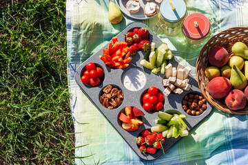 Summertime healthy picnic with fresh vegetables, nuts and fruits served in the muffin pan;...