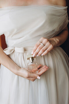 Close up of elegant perfume in a glass bottle in the hands of the bride in a wedding dress.