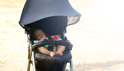 公園で黒いベビーカーに乗って寝ている赤ちゃんとコピースペース - obrazy, fototapety, plakaty