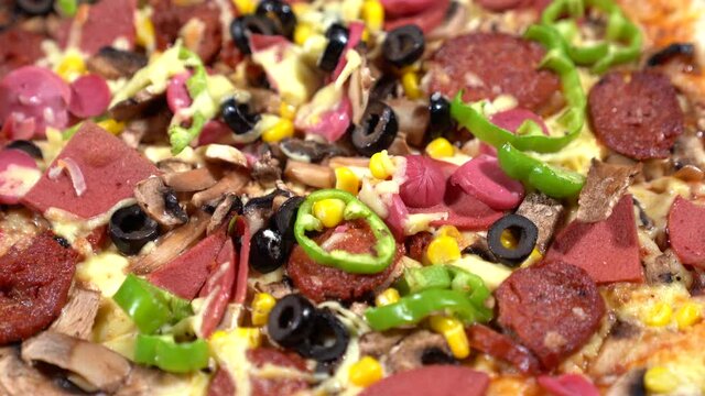 Close up view of pizza with tomato, black olives, mushrooms, bacon, paper, salami, sausage and kashar cheese turns around. 