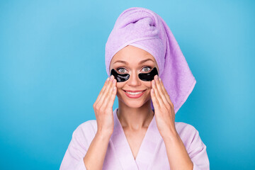 Photo of lovely young woman hold eye patches face wear violet towel turban bath robe isolated blue color background