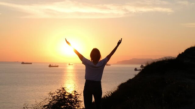 Woman silhouette spreading arms by the sea shore, sunset time. Freedom happyness concept