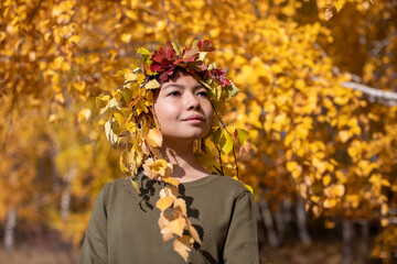 Portrait of girl wearing an autumnal foliage crown on the background of the autumn birch forest.