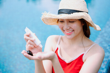 Asian woman traveler apply cream sunblock lotion at swimming pool.