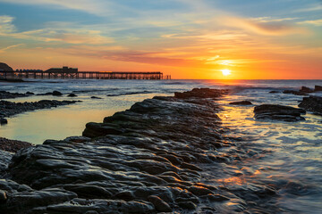 The sun rising behind the pier and the tide receding revealing the rocks on St Leonards beach...