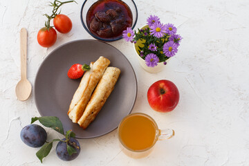 Homemade pancakes filled with cottage cheese on a plate, fruits and a cup of tea