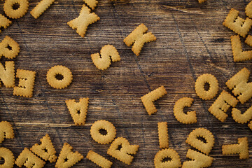 Top view photo of many alphabet cookies on a brown wooden background.