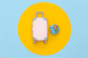 Travel concept. Mini plastic travel suitcase and globe on blue pastel background with yellow circle. Minimal style. Top view, flat lay