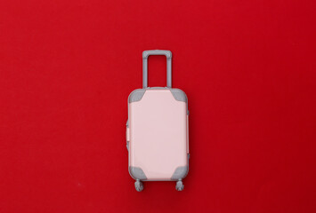 Travel concept. Mini plastic travel suitcase on red background. Minimal style. Top view, flat lay