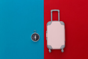 Travel concept. Mini plastic travel suitcase, compass on red blue background. Minimal style. Top view. Flat lay