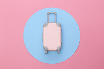 Travel minimalism. Mini plastic travel suitcase on pink background with blue circle. Minimal style. Top view, flat lay