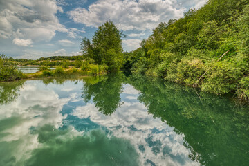 Fototapeta na wymiar Karlstrup Kalkgrav is a natural lake that formed in an old limestone quarry housing a small heaven. Clouds and vegetation reflect in the water conveying relaxation and peace of mind - Solrod, Denmark