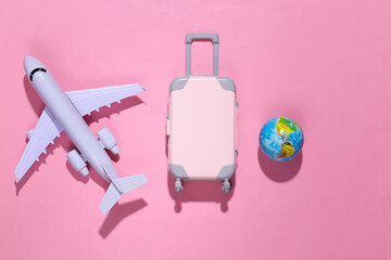 Travel minimalism. Mini plastic travel suitcase, globe and air plane on pink background with deep shadow. Minimal style. Top view, flat lay