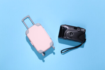 Travel minimalism. Mini plastic travel suitcase and camera on blue background with deep shadow. Minimal style. Top view, flat lay