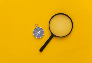 Minimalism travel, adventure flat lay. Compass and magnifier on yellow background. Top view